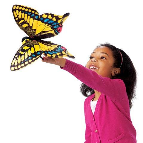 Young girl plays with butterfly puppet on finger.
