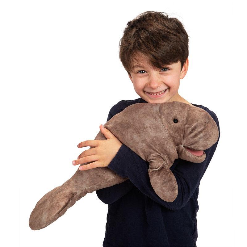 Young boy holds manatee puppet on hand and cuddles it to his chest.
