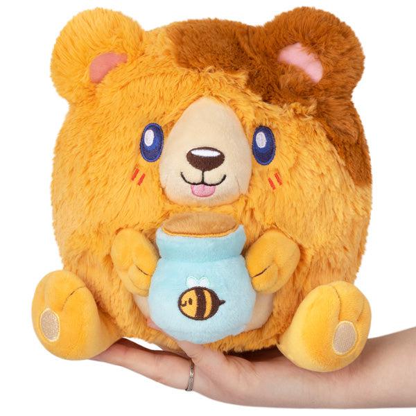 Image of the Mini Honey Bear squishable. It is a honey and brown colored bear. It is holding a blue honey pot.
