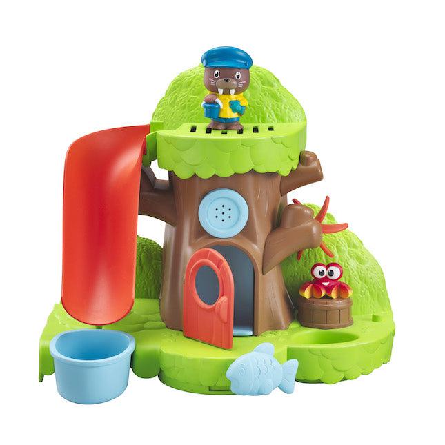 Image of the full set outside of the packing. It is a tree with a door and room inside of the trunk. From the top of the tree, there is a red slide that leads to a bucket. On the right side there is a red/yellow colored crab sitting on a barrel. On the bottom of the play set, there is a movable fish that controls the door.