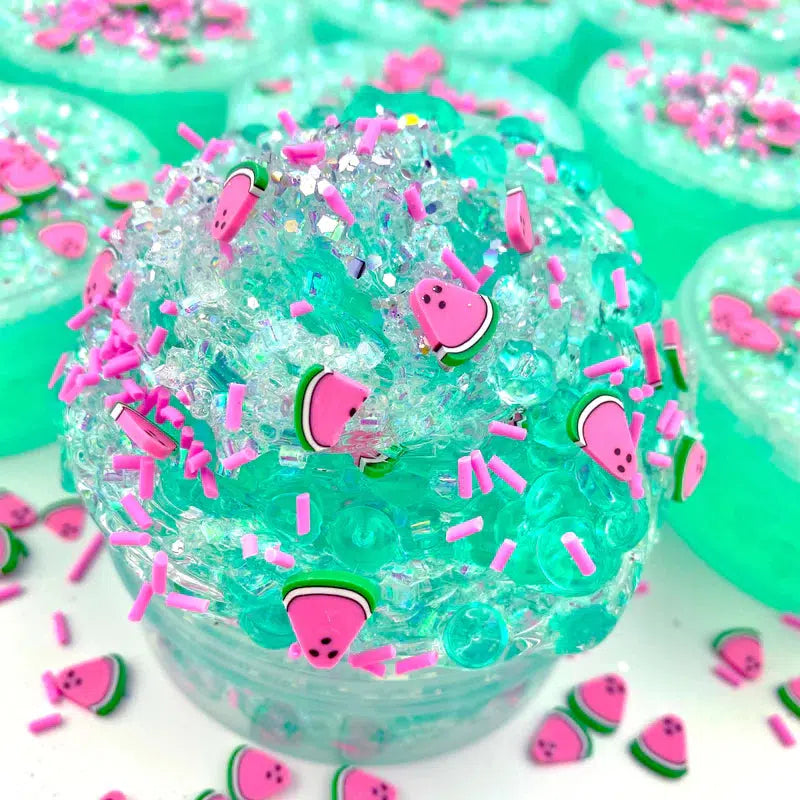 Image of the open slime. It is a dark mint/sea green. It comes with watermelon-shaped sprinkles, regular pink and sparkly sprinkles, and a watermelon charm.