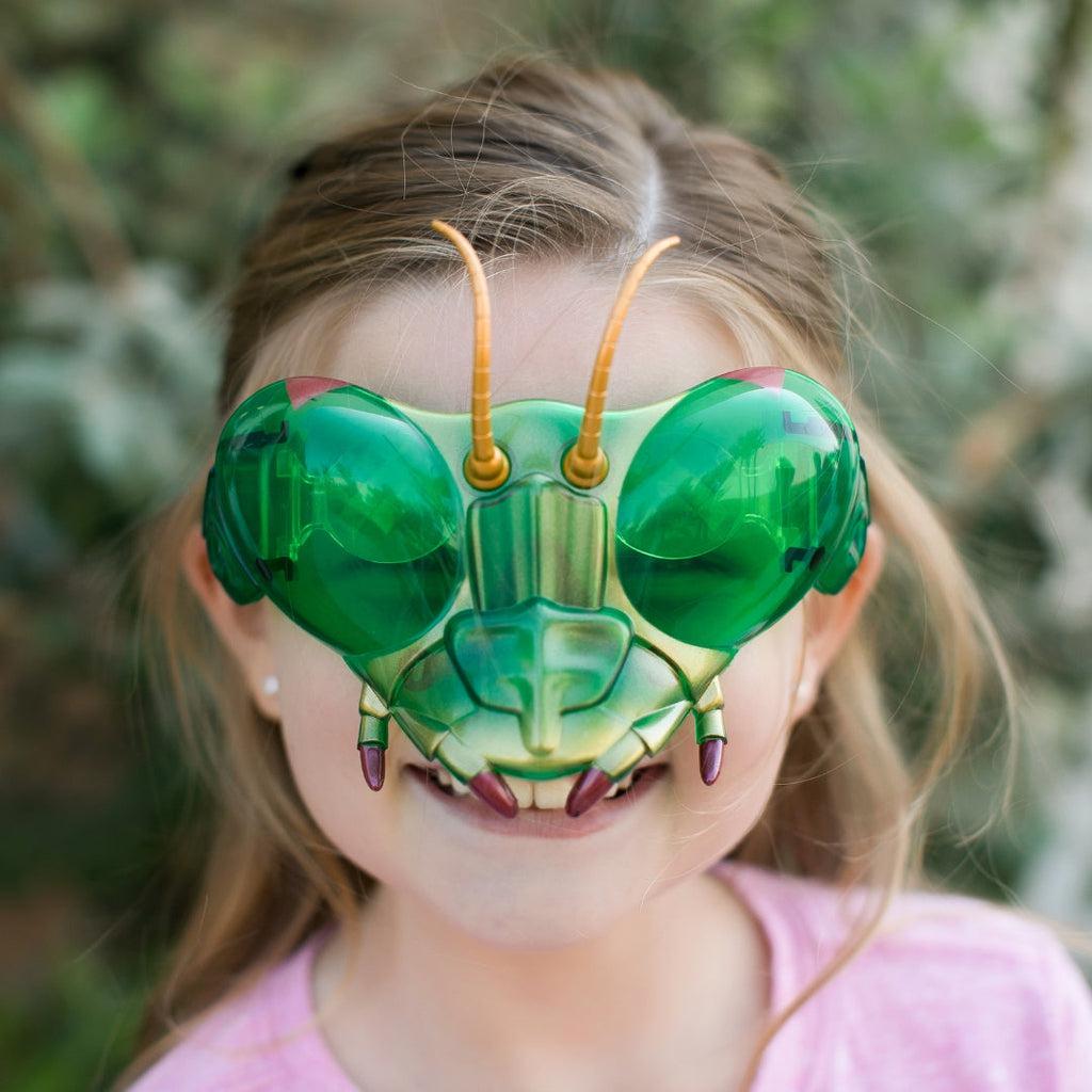 Scene of a little girl wearing the mantis goggles and smiling. The goggles are green with yellow antennae. 