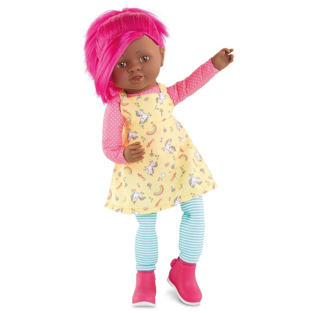 The doll has bright pink hair, a pink shirt with white dots printed all over, a dress with unicorns and rainbows on it, blue and white striped pants, and pink boots.