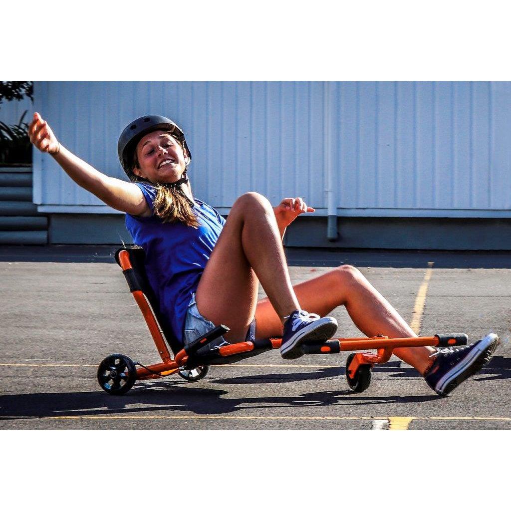 a while is smiling and waving his arm while playing on an ezyroller pro. his heet are on the bars to swivel the wheel around