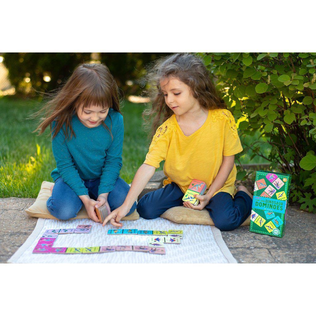 two girls are playing dominos with the dinosaur cards, showing the dominos are large in their hands, and a fun game