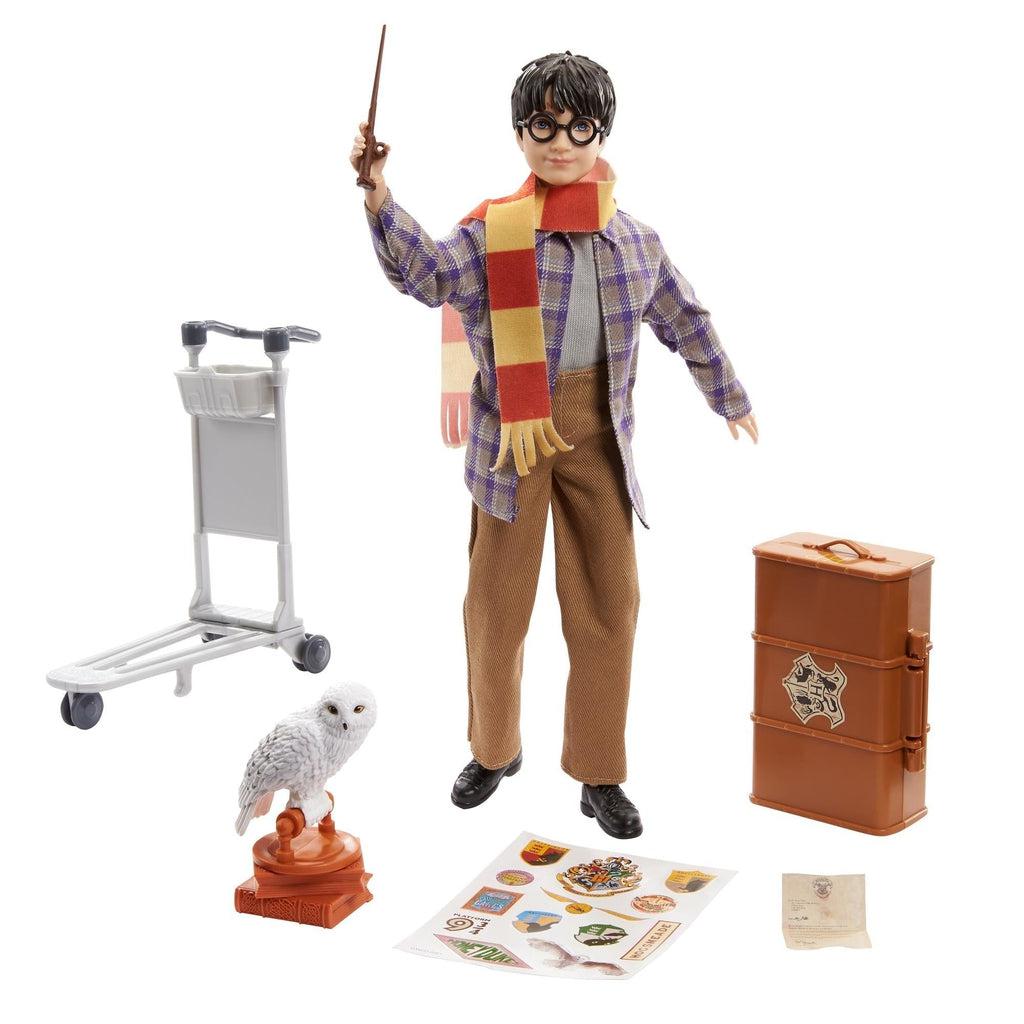 Harry Potter doll and included accessories | Doll is in black shoes, brown pants, gray shirt with a flannel print jacket and yellow/red striped scarf. | Included accessories: luggage cart, suitcase with Hogwarts logo, Hogwarts acceptance letter, stickers, and white owl with stand on books.
