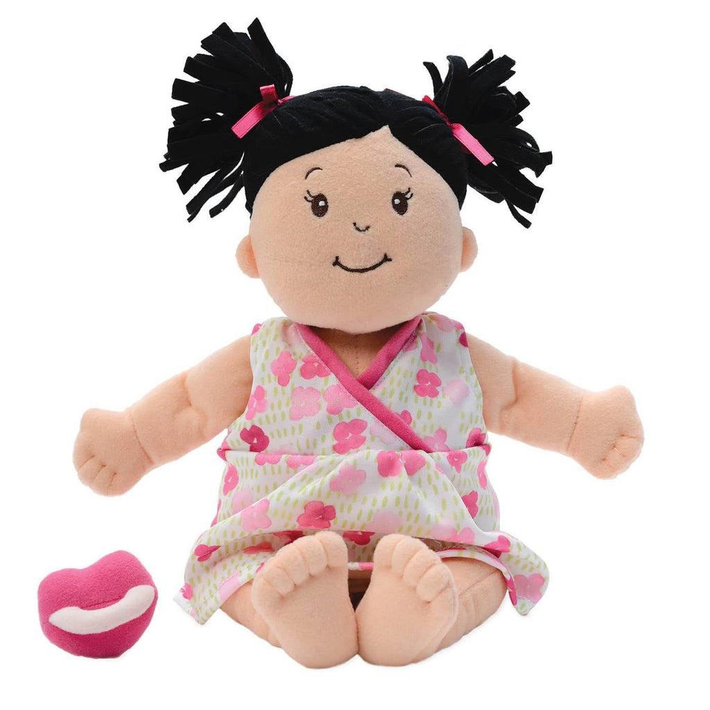 The baby stella doll is shown sitting net to it's pacifier. The doll has black hair that is made up of thick strips of fabric. The doll is also wearing a white dress with pink and red flowers printed on it