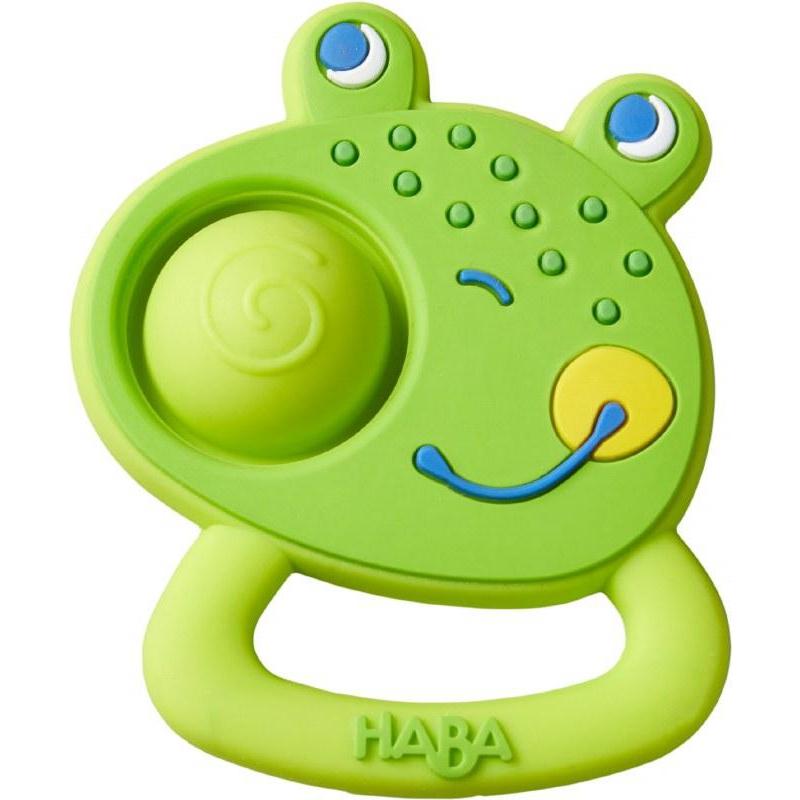 Image of the teething toy outside of the packaging. It is a face of a frog with a smile and dimples. One of the dimples is rubber and puffy with a spiral on the top.