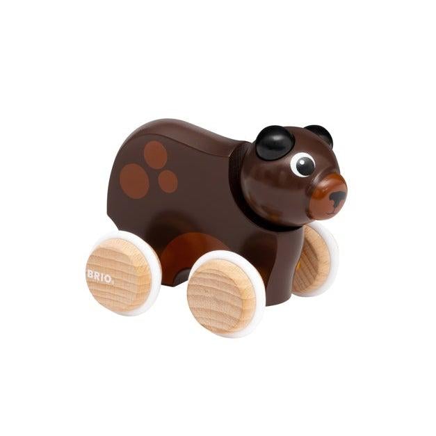 Side view of the toy. Brown bear with 3 lighter brown spots on its flank. Has 4 light brown, wood-textured wheels.