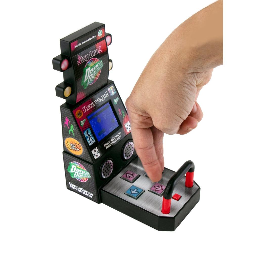Image of two fingers playing the World's Smallest Dance Dance Revolution machine. The machine has lights, a screen, a speaker that plays music, and blue and pink colored arrow buttons.
