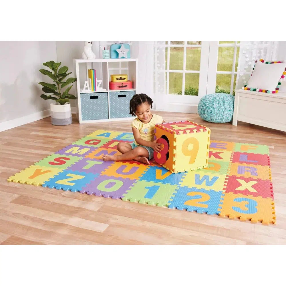 A baby is playing on the soft puzzle mat while part of the mat has been shaped into a cube for the baby to play with and pull out the numbers or letters in the tile block. 