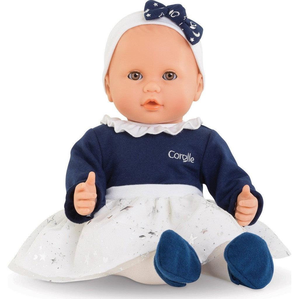 A baby doll in a dress with a blue top section and white skirt section, a white headband with a blue star decorated bow, and blue socks.