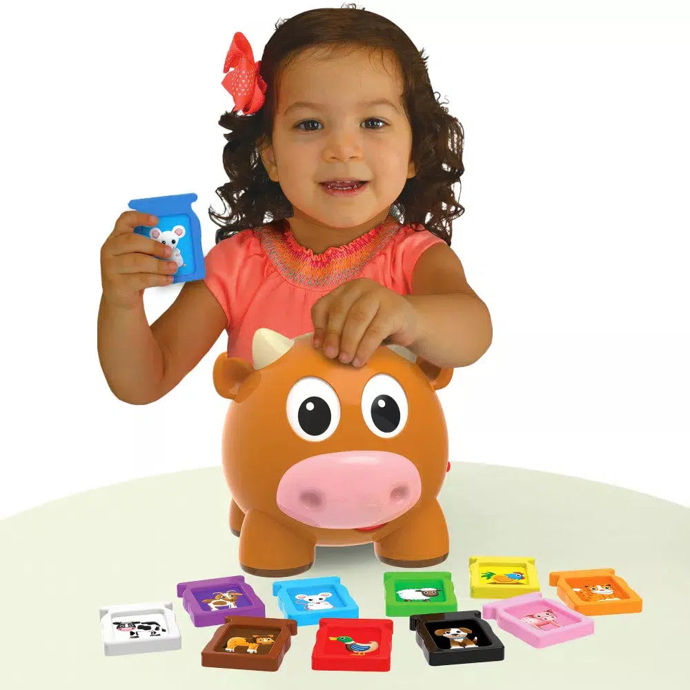 a child is placing a sound into the top of the cow to learn about animals. 