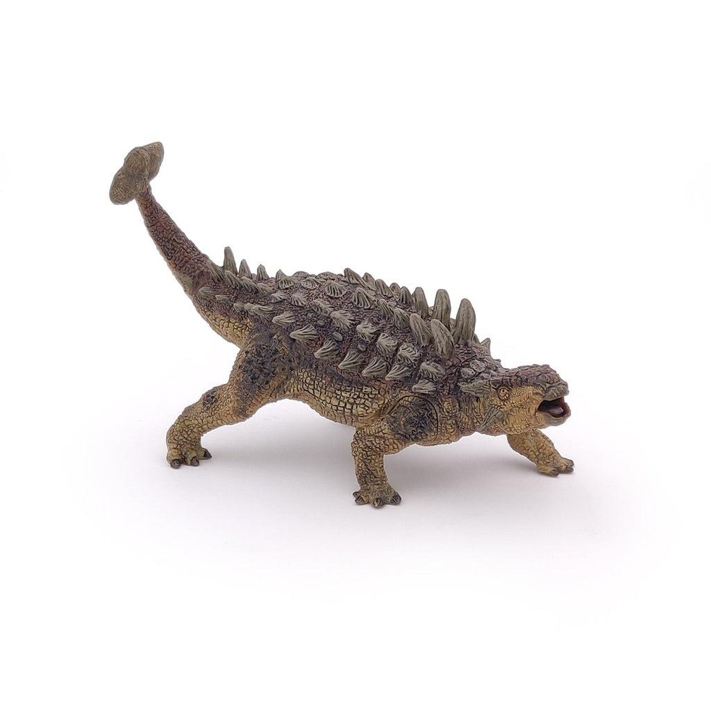 Image of the Ankylosaurus figurine. It is a smaller tan and brown dinosaur with spikes all along its back. It has a tail with a big hammer spike on the end of it.