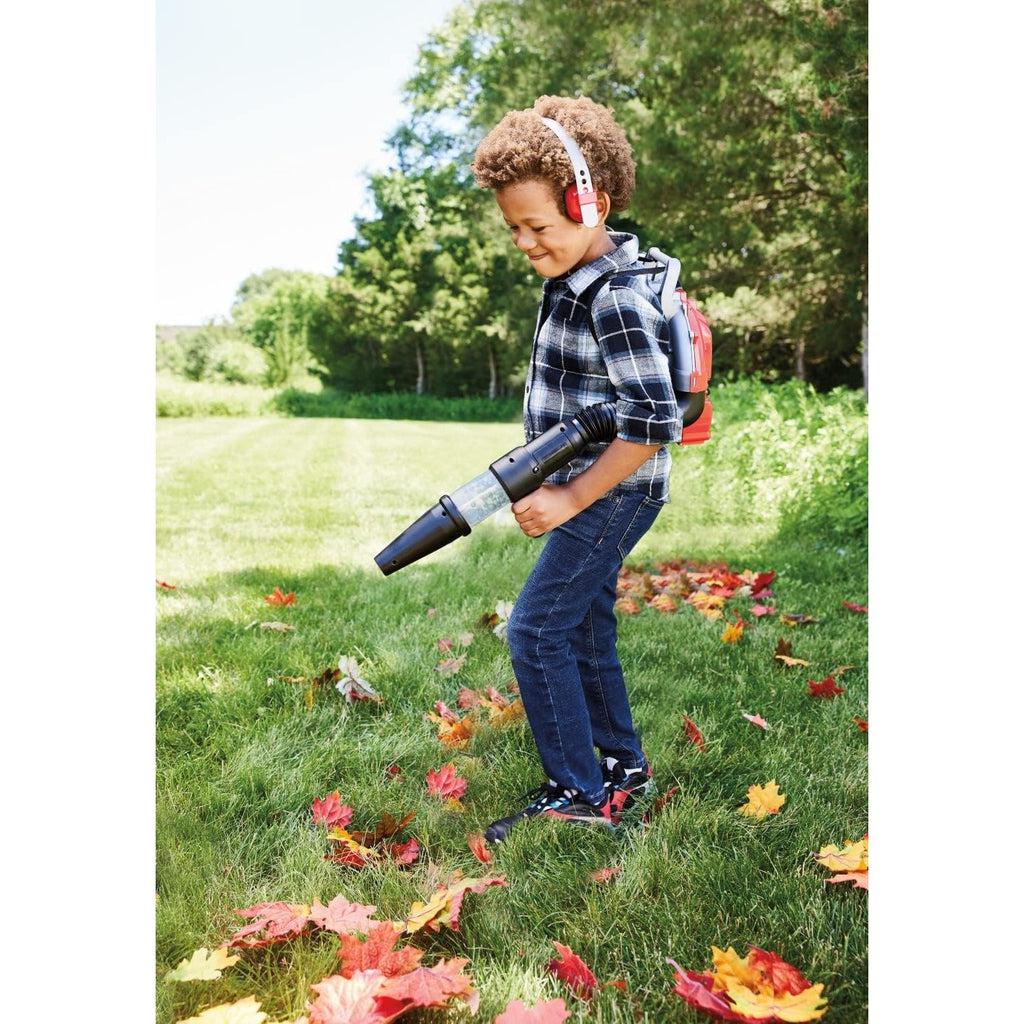 picture of a boy pretending to blow the leaves in his yard, he is working hard and playing hard. 