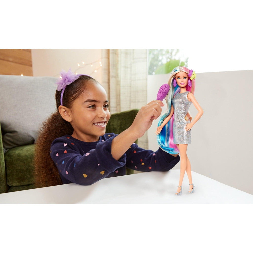 Scene of a little girl smiling while brushing Barbie's hair.