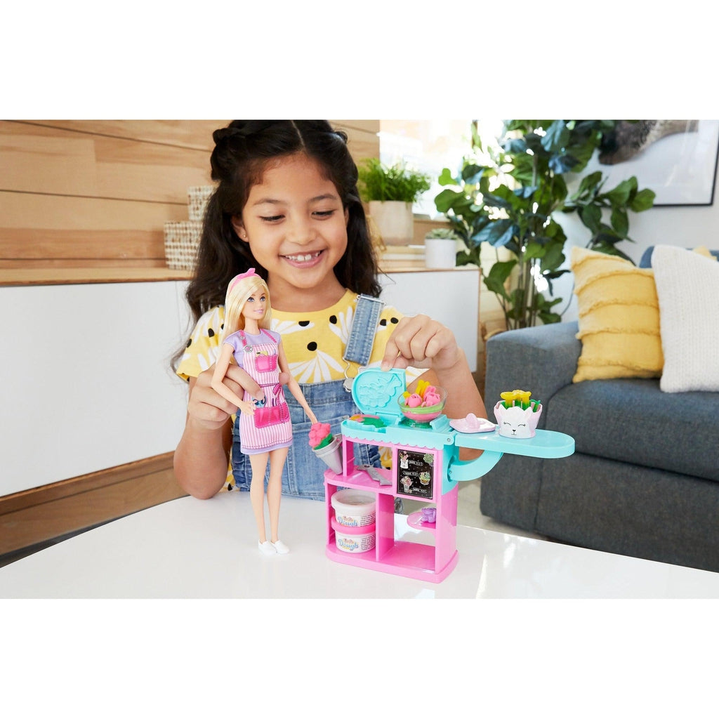 Scene of a little girl holding Barbie and making flowers while smiling.