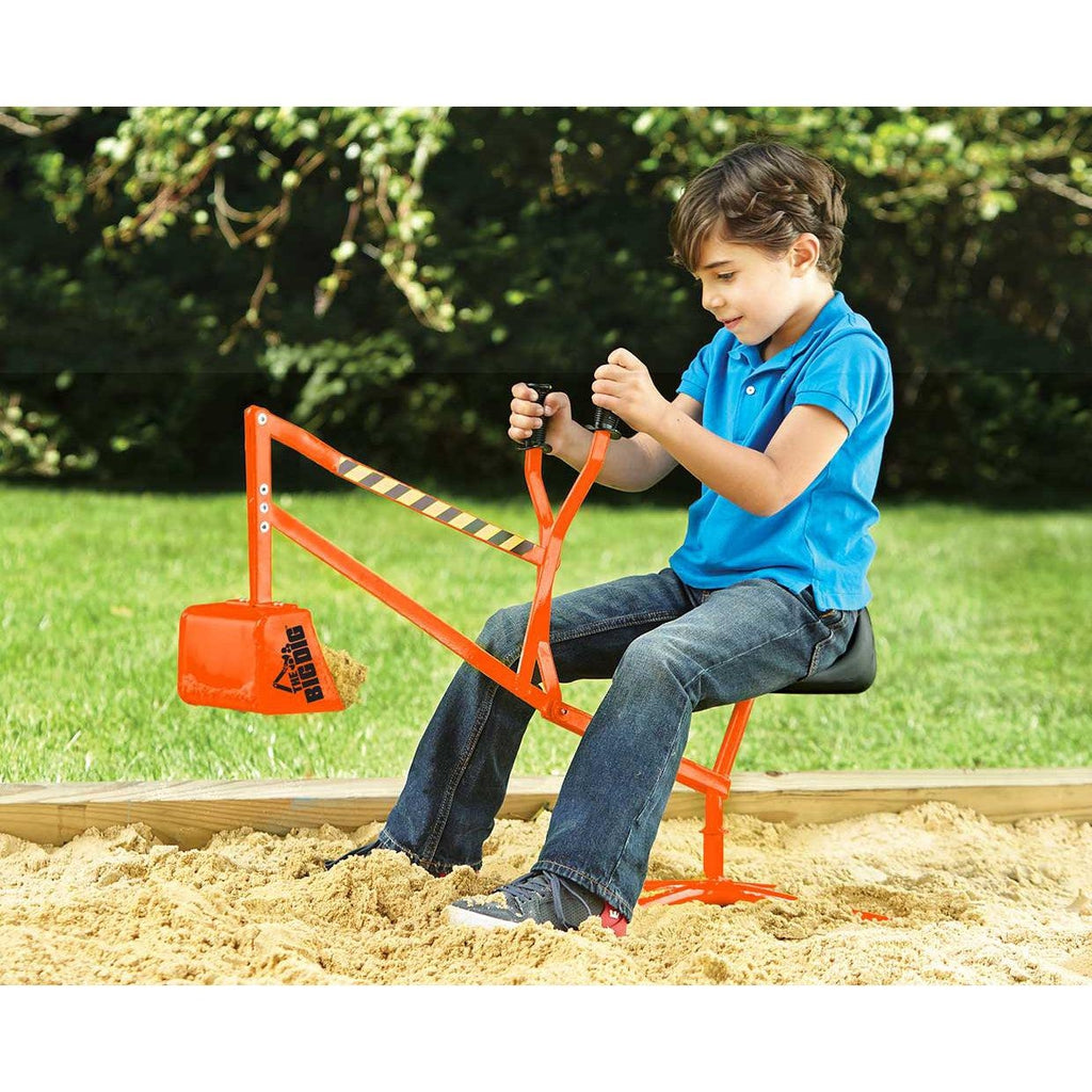 Scene of a little boy sitting on the Big Dig toy and scooping up some sand.