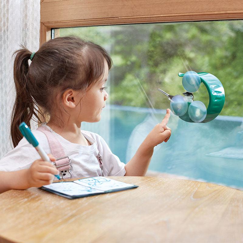 image shows a small child pointing to the bird feeder cuction cupped to the window while a bird eats some seeds.