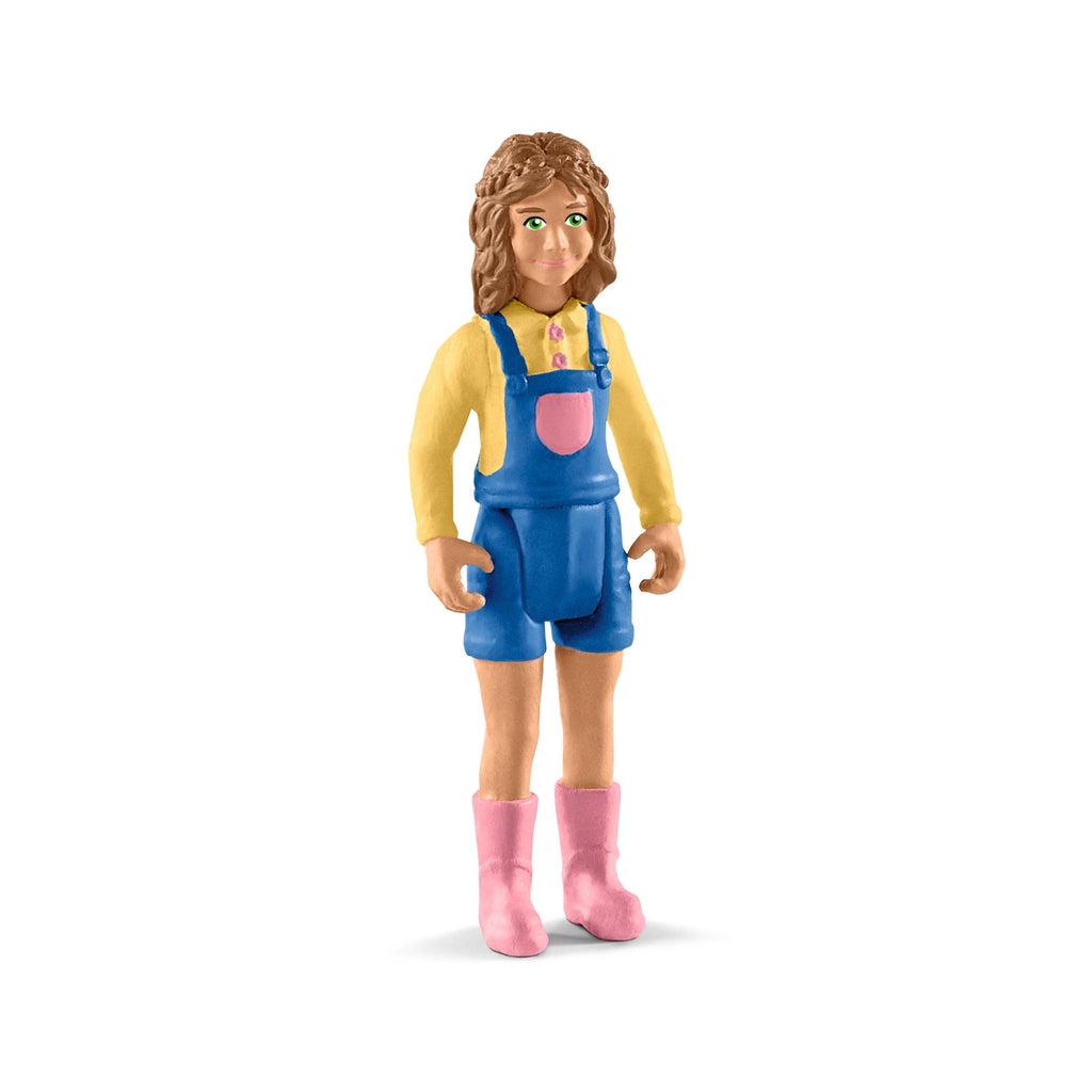 Close up of the little girl figure. She is wearing a yellow shirt and blue overalls. She has pink rain boots and long wavy brown hair.