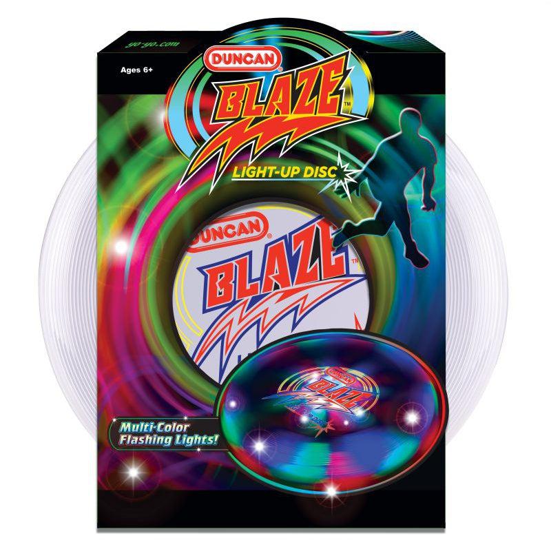 Image of the packaging for the Blaze Light-Up Disk. The disk is partially covered with a cardboard sign with the name of the toy and company on it. There is also a silhouette of a man kicking the disk on the front. The disk itself is clear.
