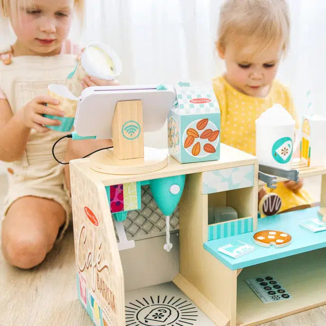 Scene of two little girls playing with the play barista shop. They are concentrating on creating the coffee and pastries.