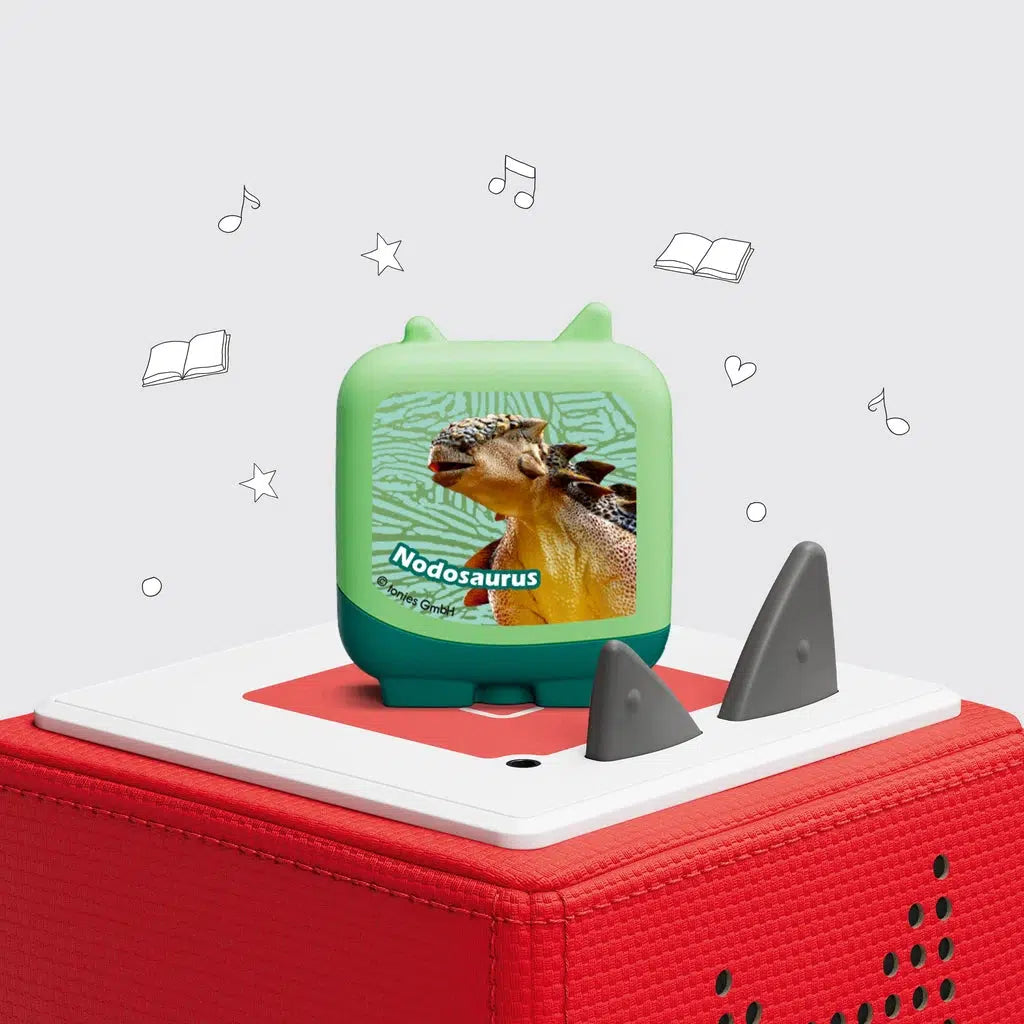 One of the 4 included clever tonies is shown on a toniebox. The figure is a green square with feet and tonie ears. The front of it is labeled "nodosaurus" with a picture of that dinosaur on it.