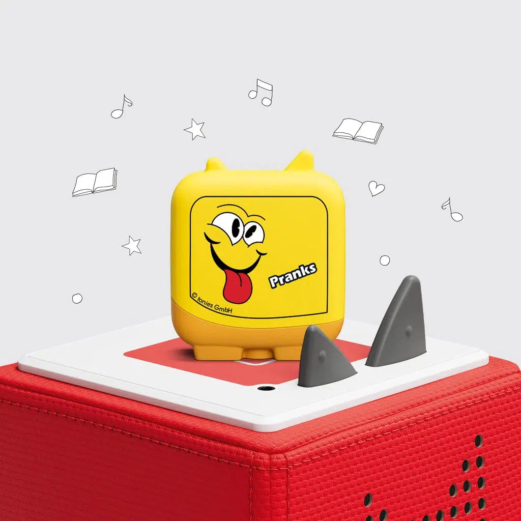 one of the 4 included clever tonies is shown on a toniebox. The figure is a yellow rectangle with feet and tonie ears, the front has a face sticking out it's tongue and the label "Pranks".