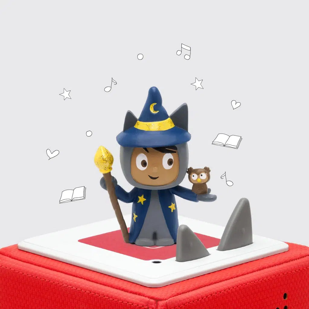 The tonie figure is shown on a toniebox. The figure is a young boy in a grey tonie character suit with the tonie ears. He also has a wizard hat and robe, a magic staff, and a small owl in his other hand.