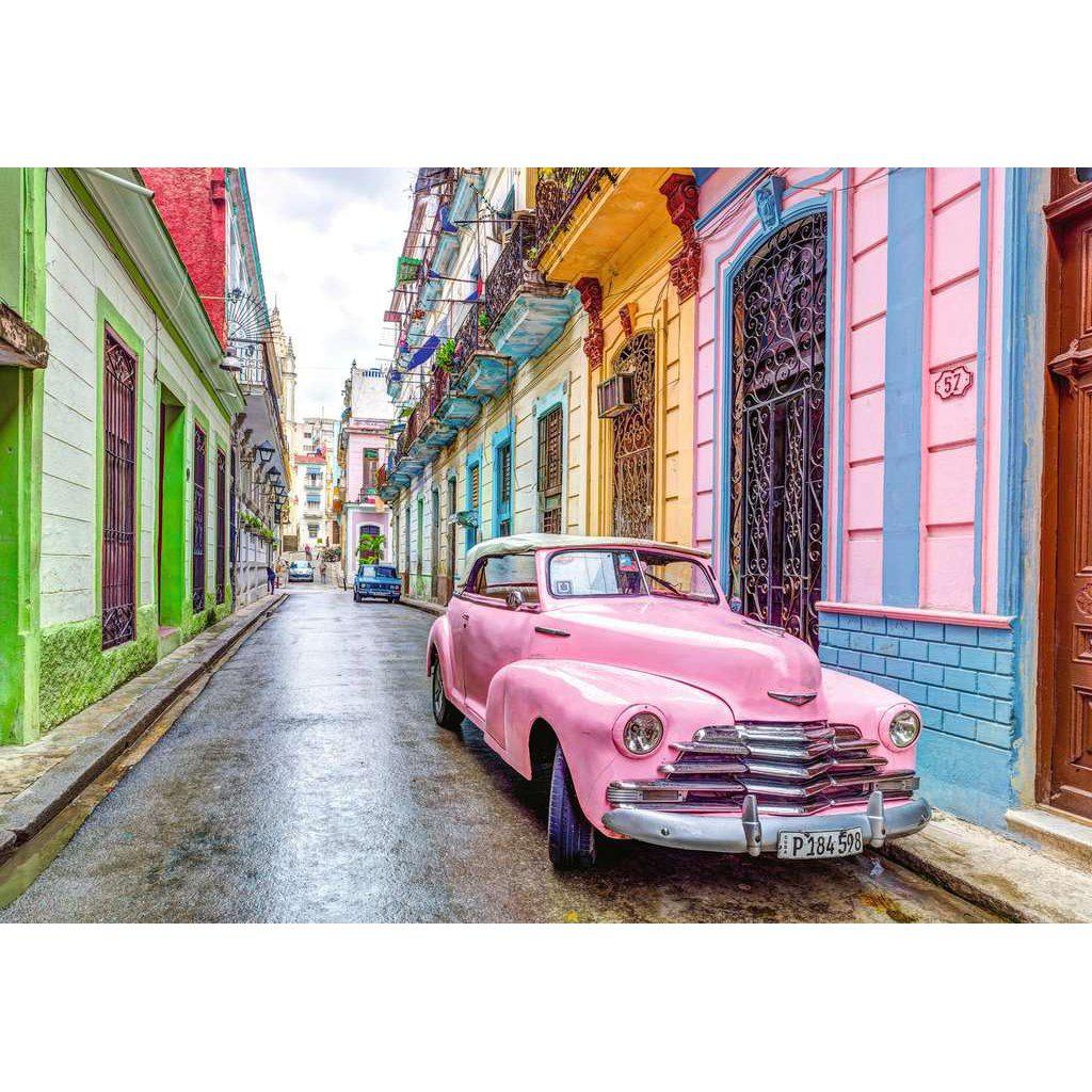 Image of the finished puzzle. It is a picture of a street in Cuba. Each of the apartments are a different bright color and there is a classic pink car out on the street.