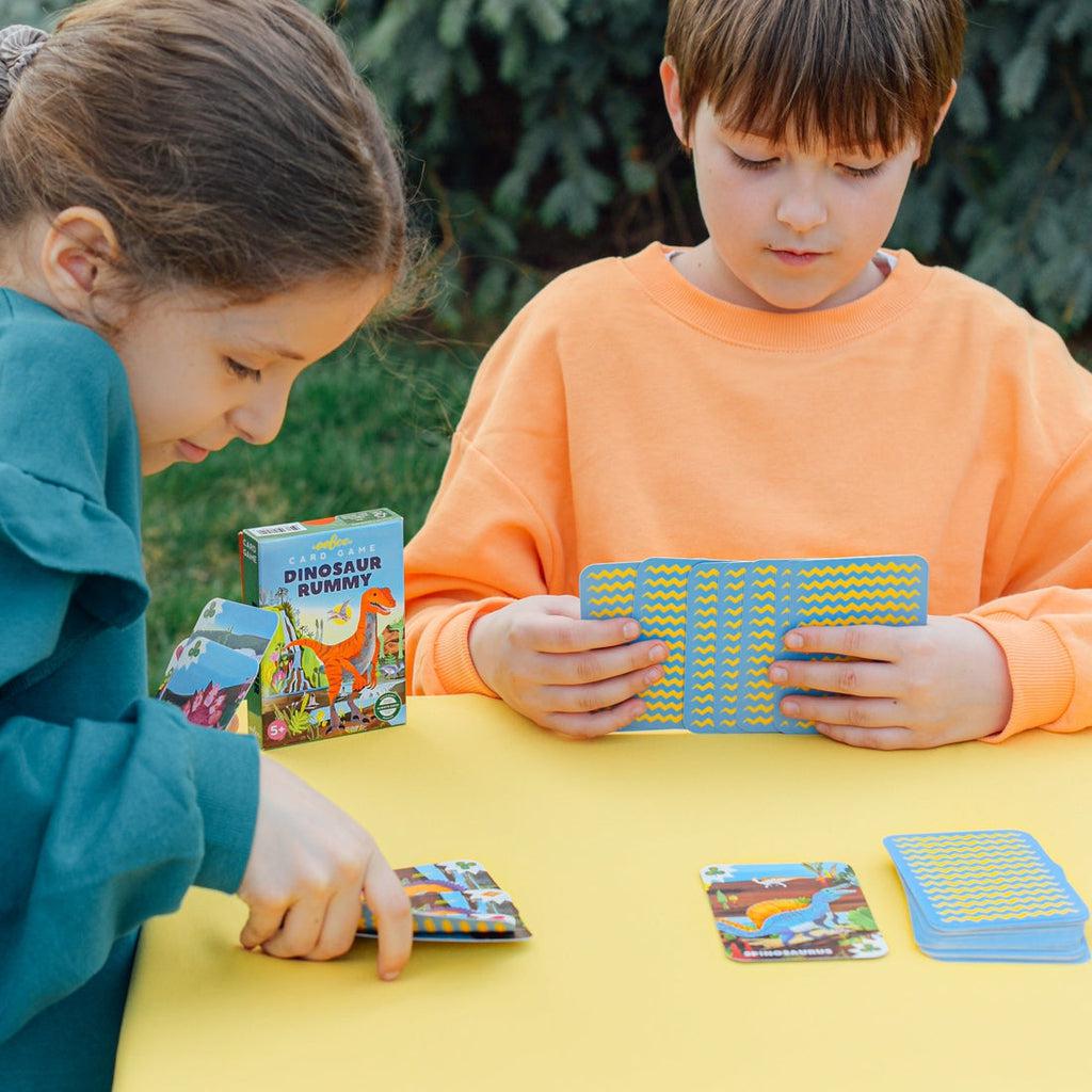 another shot of two kids playing rummy on a table, looking at the dinosaur art