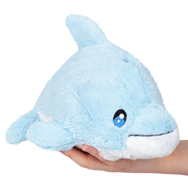 Image of the Dolphin Snacker squishable. It is a light blue dolphin plush with a white belly.