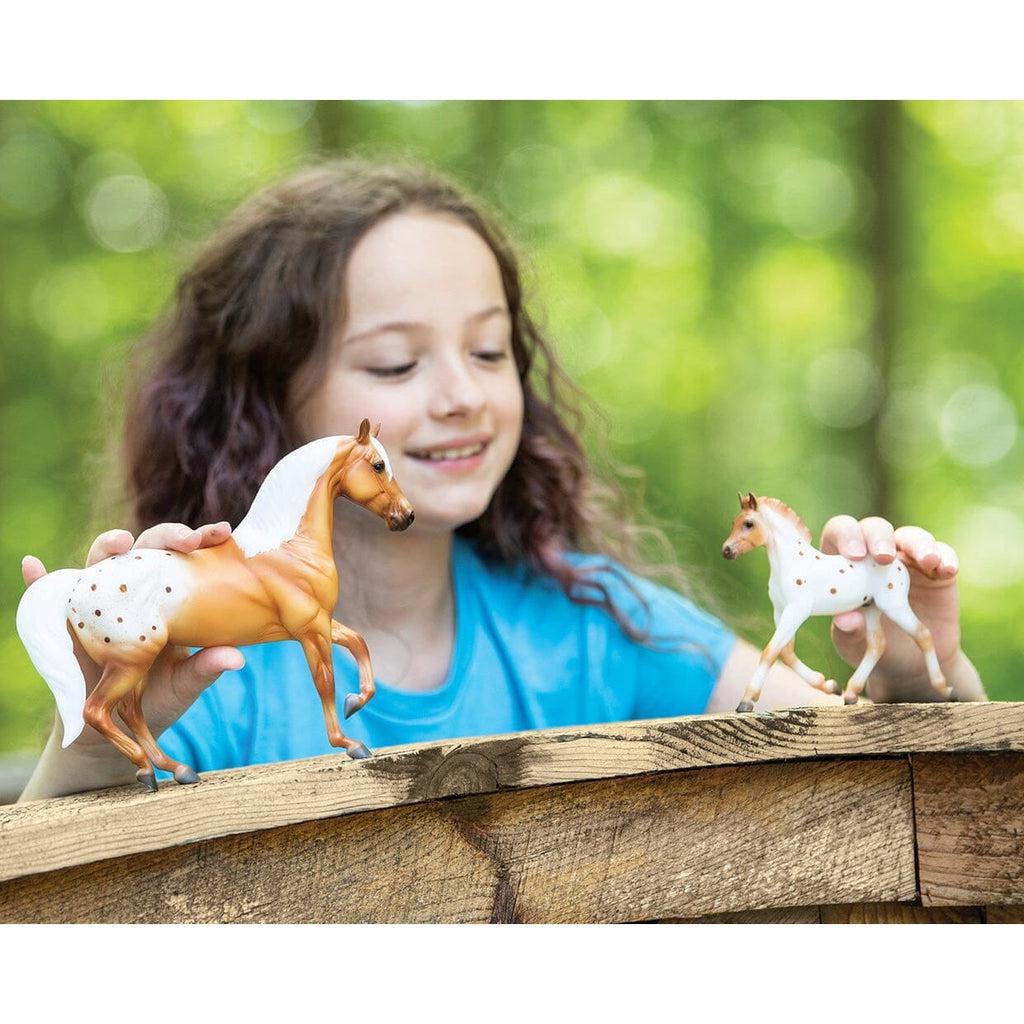 Scene of a little girl playing with both of the horse figurines.
