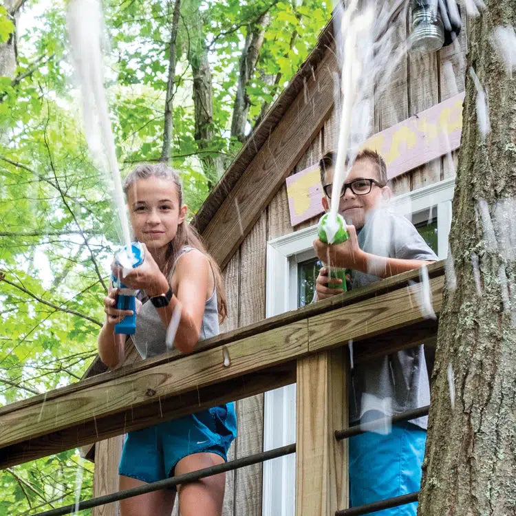 2 kids in a treehouse shoot foam at the camera from their foam guns