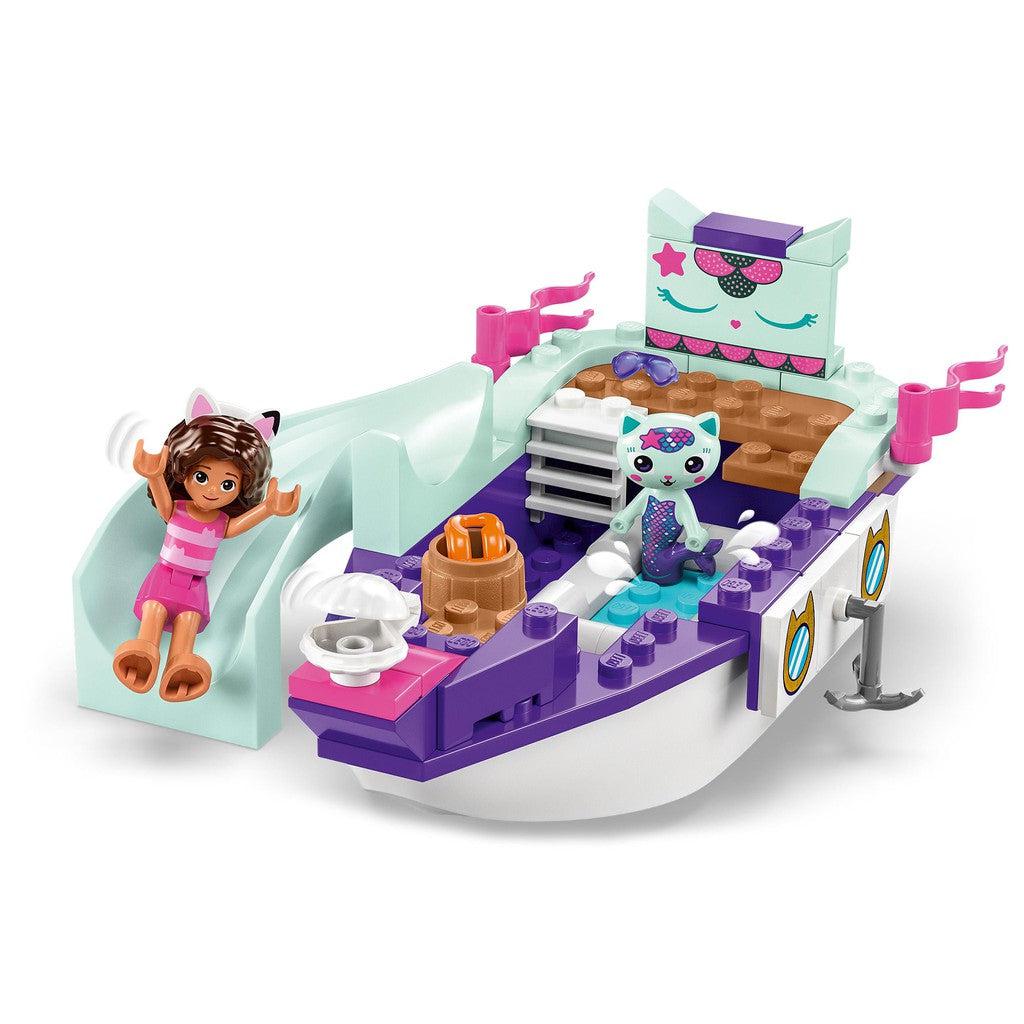 image shows ther MerCat ship with a mermaid cat on board, the deck is purple and there is a white slide on the side of the boat.