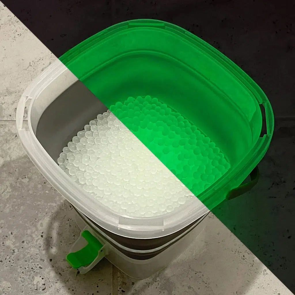 Image split diagonally with one half showing the normal color of the gellets being a cloudy white, other half shows them in the dark where they glow a bright green.