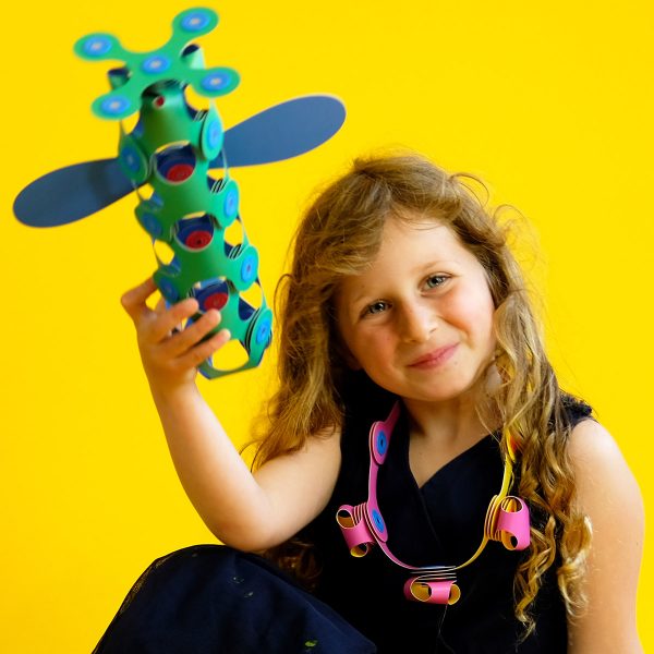 Young girl proudly displaying a colorful Clixo construction against a yellow background.