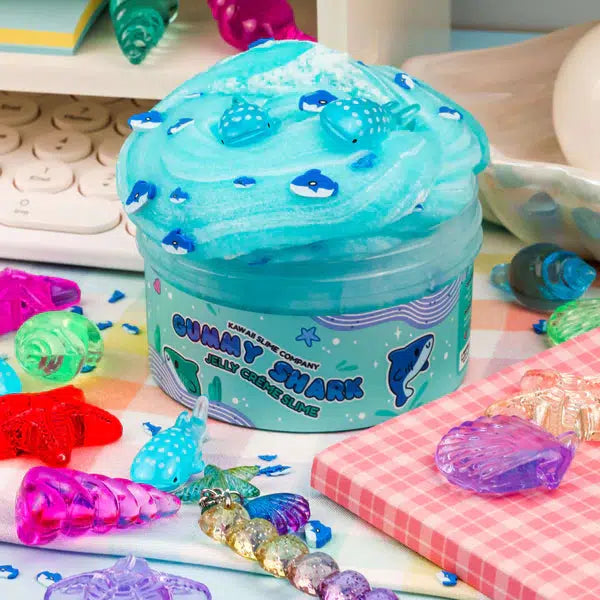 Image of the opened slime. It is a bright blue color with an interesting mixed texture. It comes with tiny shark shaped sprinkles and two shark charms.