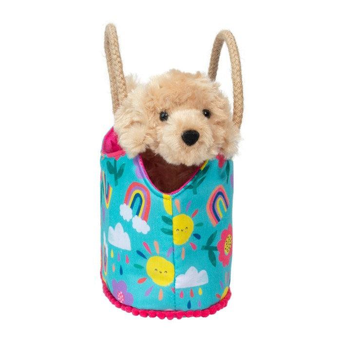 this image shows a light brown colored dog  stuffed animal in a small purse that is blue with rainbows and suns with a happy face.
