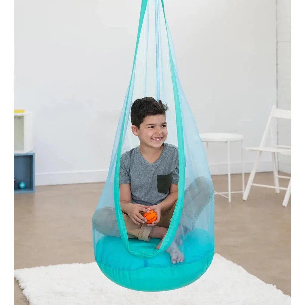 image shows a boy in the huggle pod. The pod is a round padded hanging chair that has a mesh around the person inside