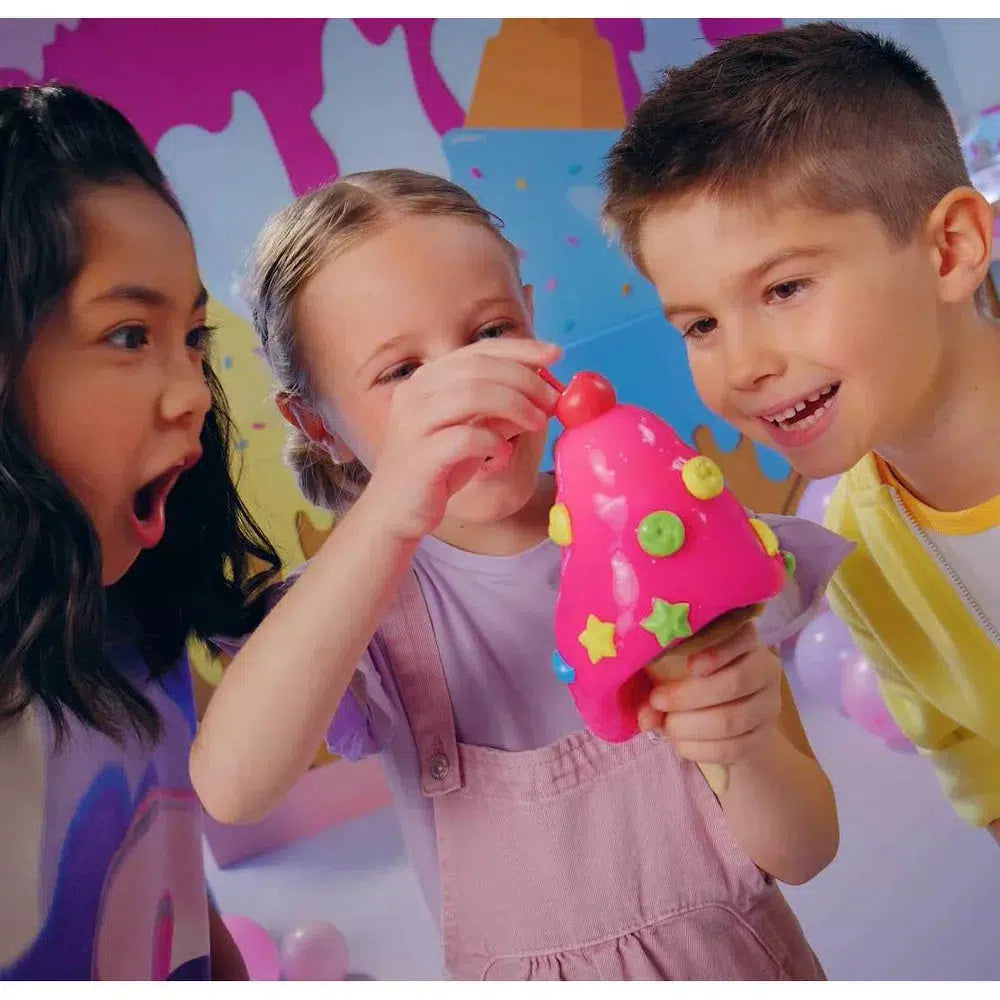 a child is putting a cherry piece on top of the ice cream slime while other kids are cheering her on