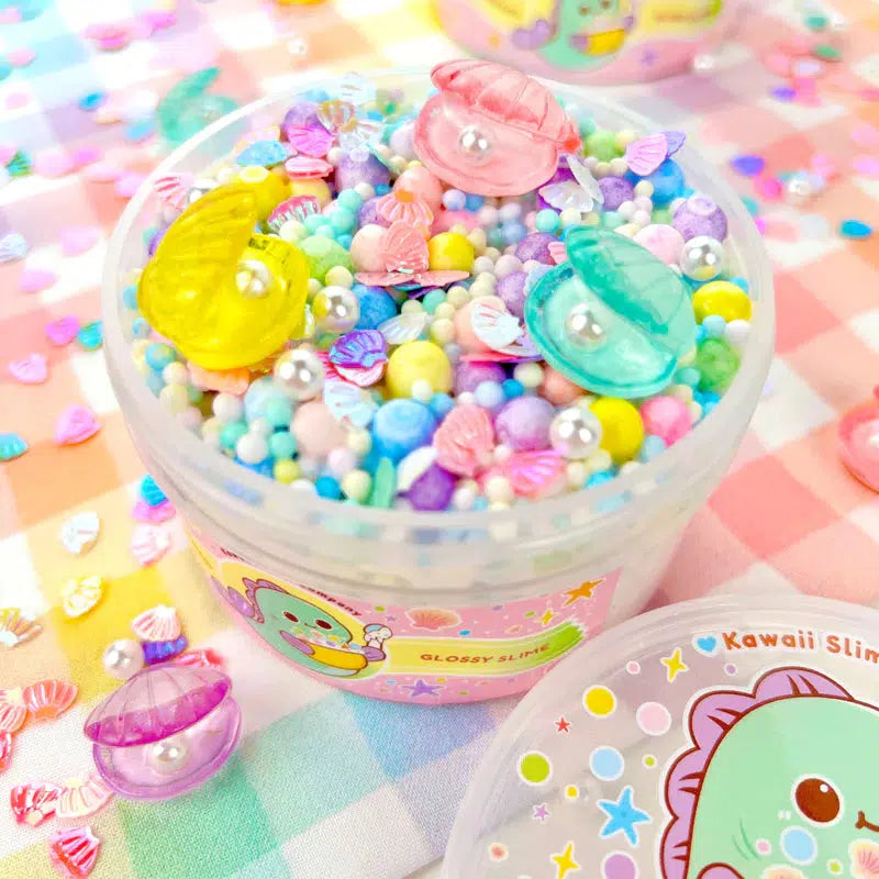 Image of the open slime. It is a white slime with rainbow foam beads inside. It comes with pearl beads and irridescent clam charms to top the slime.