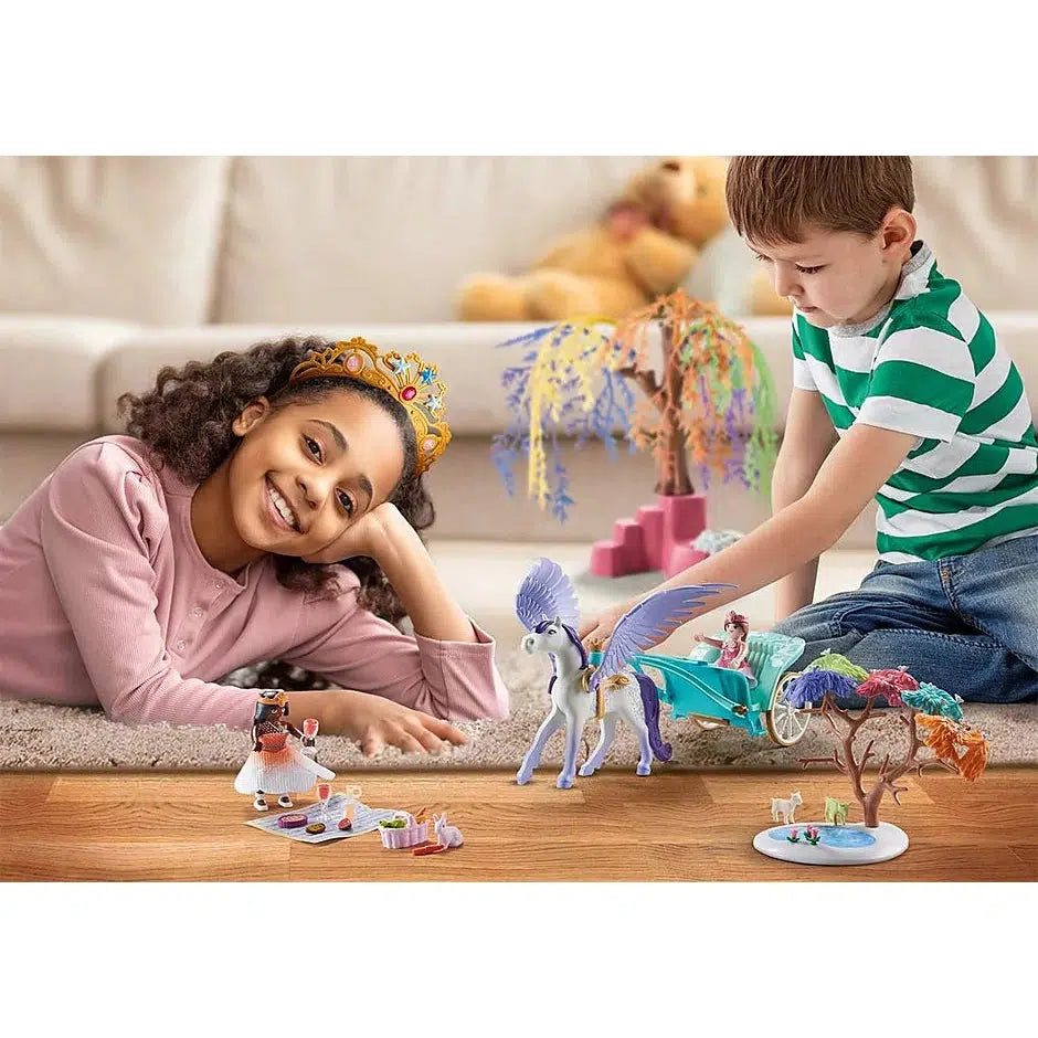 a boy and a girl are playing with the set, the Pegasus is pulling a princess on a cart while another princess is getting ready for a picnic. the boy is pushing the pegasus around and the girl is smiling and wearing a tiara.  