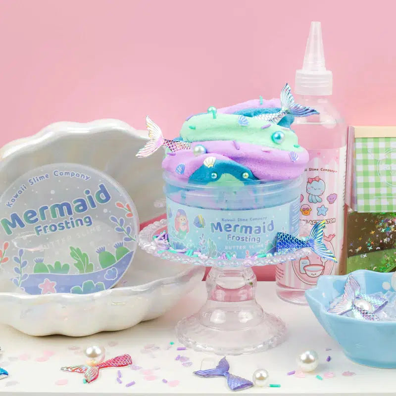 this image shows the mermaid frosting slime on a cake mount, the slime is in its container, raised ip with mermaid tails poking out of it