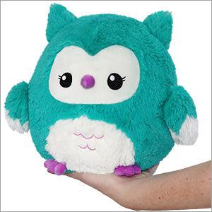 A plush turquoise and white owl toy with large eyes and a small purple nose, epitomizing owl babyhood, resting on a human hand.
