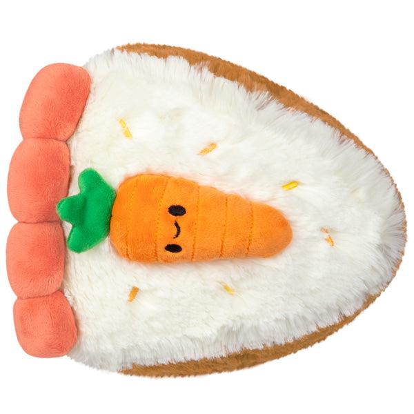 Top view of the plush. There is a smiling carrot sitting on top of the slice of carrot cake.