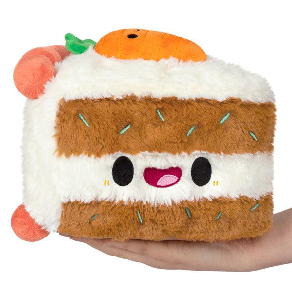 Image of the Mini Carrot Cake squishable. It is a brown cake with white icing. It has small green embroidered lines in the brown cake section.