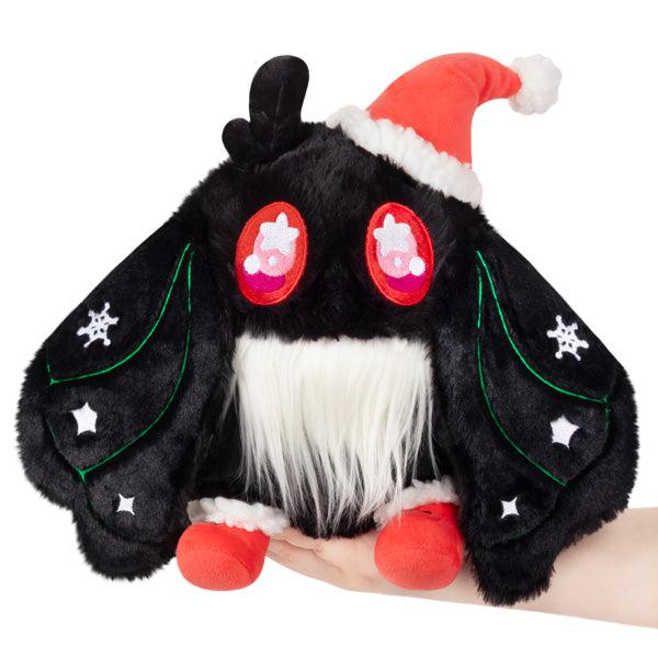 A Festive Baby Mothman plush featuring a black body adorned with red, green, and white motifs, held in a hand and topped with a Santa hat.