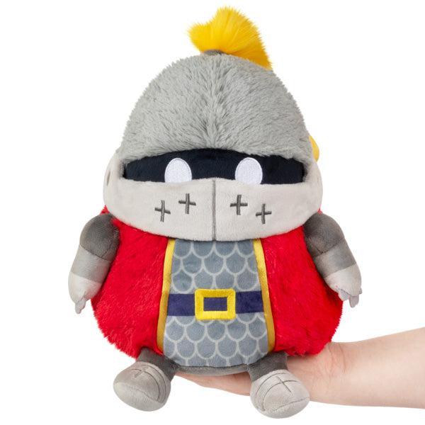 A plush toy resembling a knight, featuring gray armor, a red tunic, and a quirky expression.