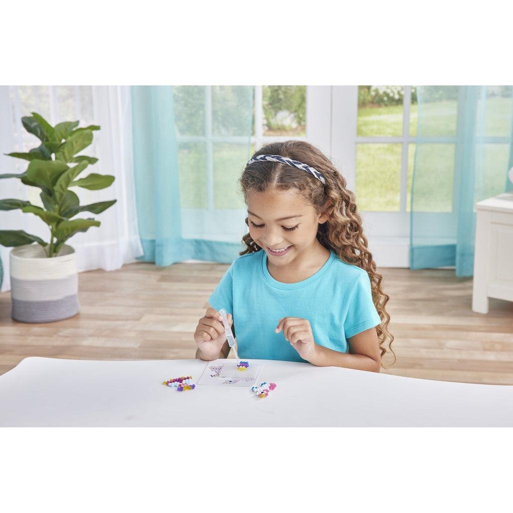 picture of a young child playing with aquabeads, using the dropper to place a bead on the tray